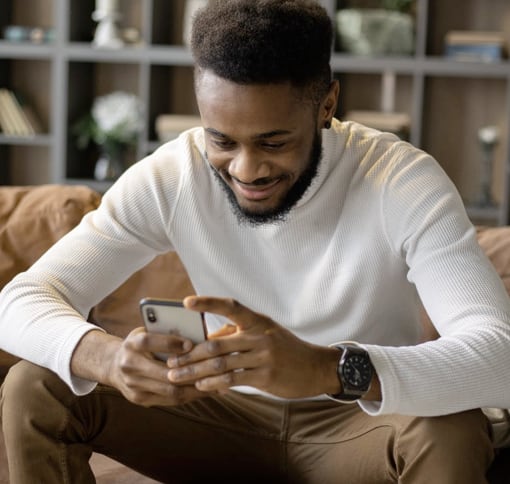 a man siting on a couch with a phone in his hands and smiling while looking at it