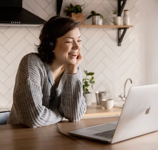 a woman inside her kitchen smiling during a video call on a MacBook