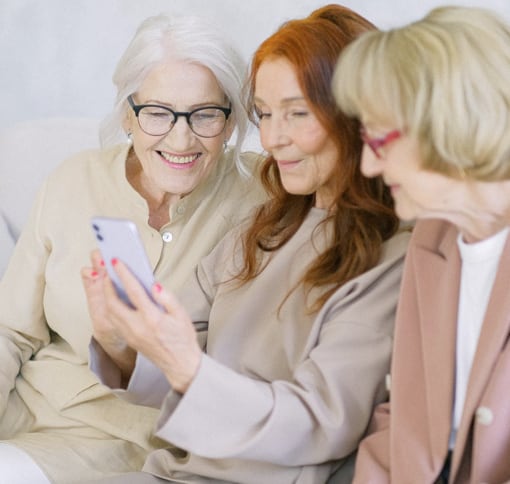 three older women smiling while they are looking on a phone