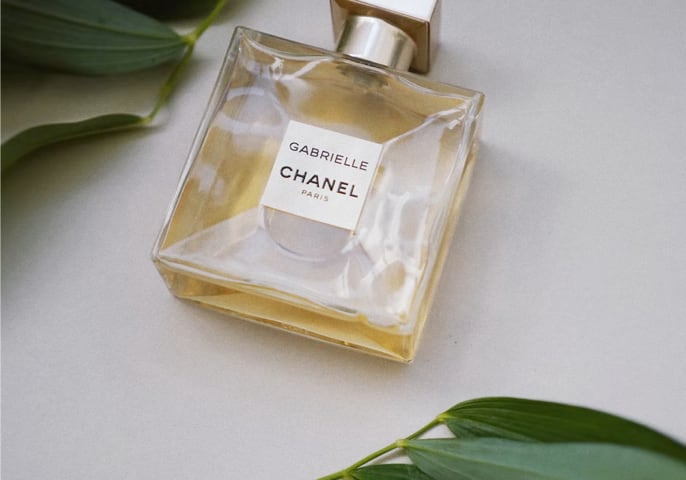 Gabrielle Essence parfum bottle laying flat on a table with green leaves above and bellow it