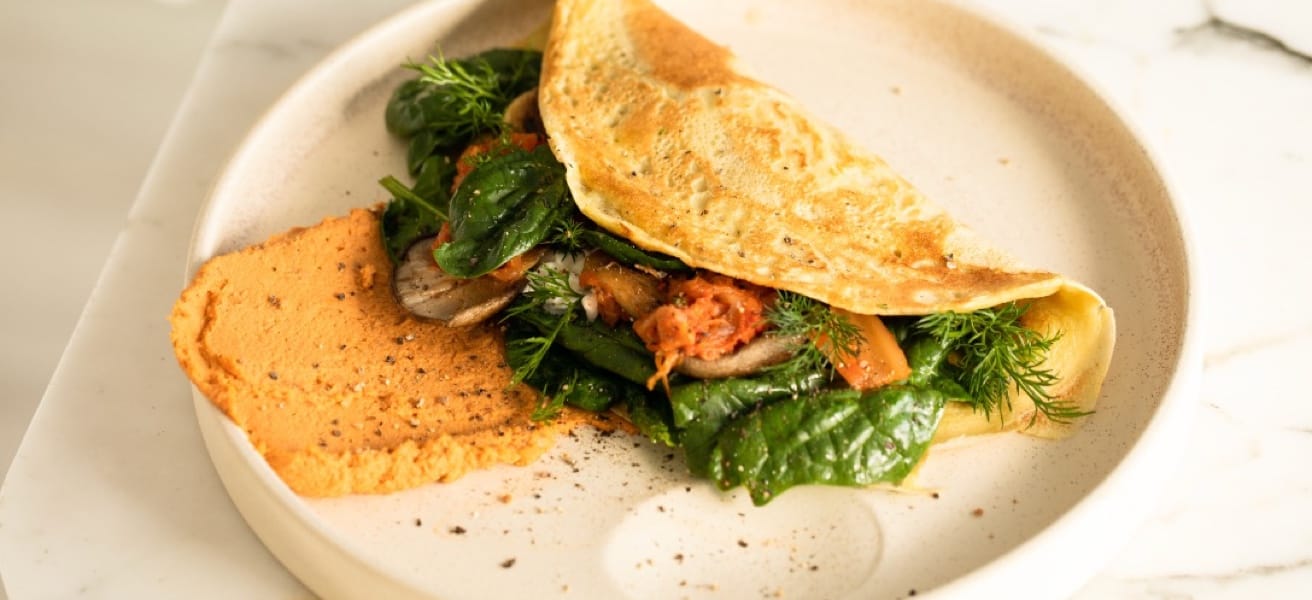 a wrapped omelette filled with dill, spinach leaves and other vegetables, on a white plate sitting on the table