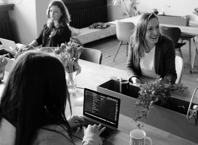 women inside an office working on their laptops at a face to face desk